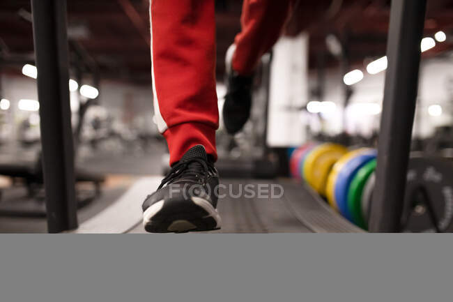 Crop atleta masculino anónimo en ropa deportiva y zapatillas de deporte corriendo en la cinta de correr durante el entrenamiento de fitness en el gimnasio moderno - foto de stock