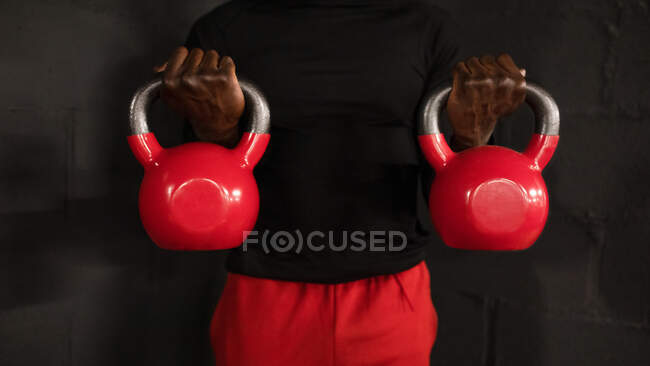 Crop unrecognizable African American male athlete in sportswear lifting heavy kettlebells while doing biceps exercise during workout in gym — Stock Photo