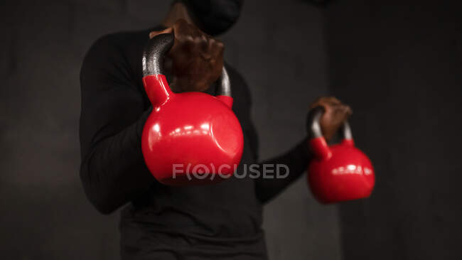 Crop unrecognizable African American male athlete in sportswear lifting heavy kettlebells while doing biceps exercise during workout in gym — Stock Photo