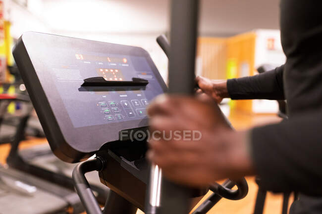 Vista laterale dell'anonimo sportivo afroamericano che fa cardio workout su una macchina ellittica nella moderna palestra — Foto stock