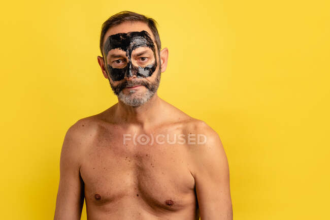 Männchen mittleren Alters zeigt schwarze Maske auf dem Gesicht, während sie in die Kamera auf gelbem Hintergrund schaut — Stockfoto