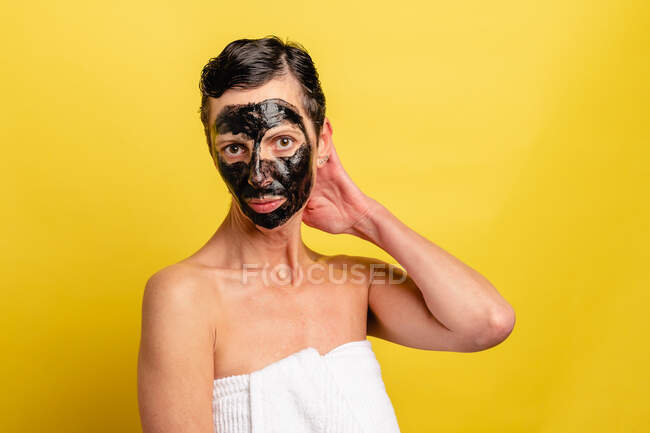 Жінка середнього віку з чорною шкірою від маски стоїть на жовтому фоні студії дивлячись на камеру — стокове фото