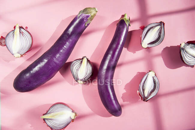 Top view still life composition with fresh whole eggplants and halved red onion bulbs placed on pink background with light and shadows — Stock Photo