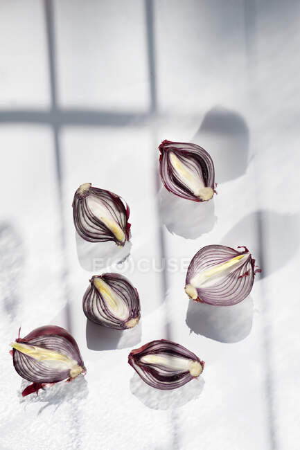 Vista superior de la composición de estilo minimalista con bombillas de cebolla roja a la mitad dispersas aleatoriamente sobre fondo gris claro - foto de stock