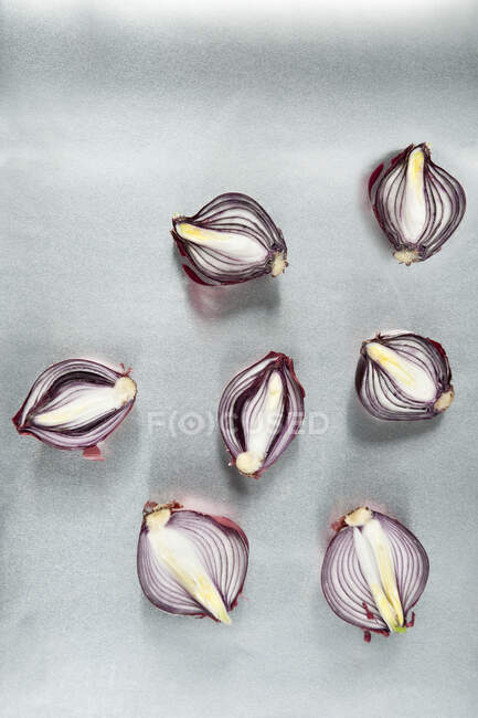 Composizione in stile minimalista vista dall'alto con bulbi di cipolla rossa dimezzati sparsi casualmente su sfondo grigio chiaro — Foto stock