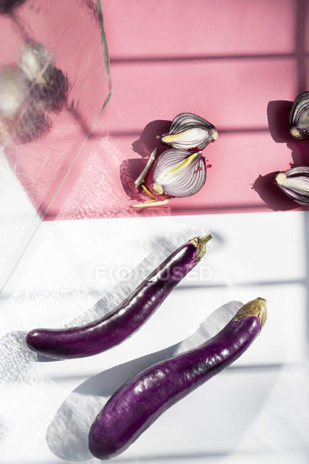 From above still life composition with fresh whole eggplants and halved red onion bulbs placed on pink background with light and shadows — Stock Photo