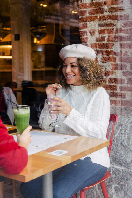 Ritratto di una donna afro con un cappello che beve un frullato dentro un bar — Foto stock