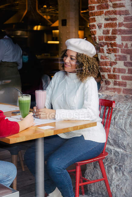 Retrato de uma mulher afro com um chapéu bebendo um smoothie dentro de um bar — Fotografia de Stock