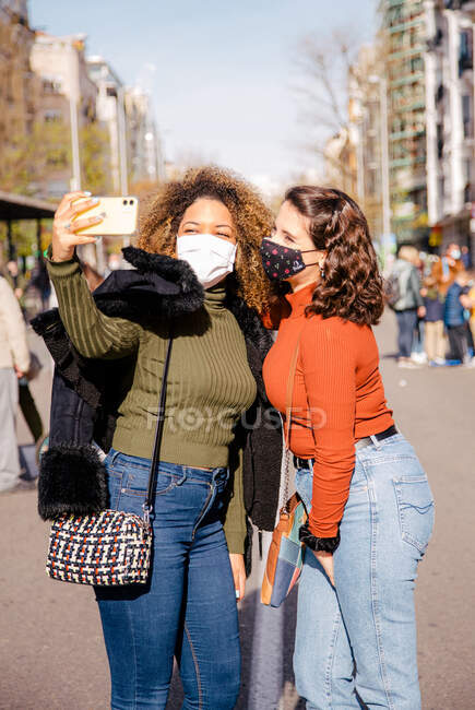 Dois amigos fazendo um auto-retrato na rua em um dia ensolarado enquanto usavam máscaras — Fotografia de Stock