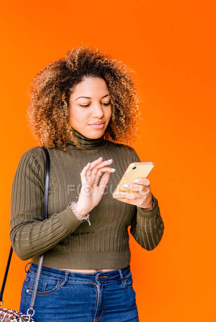 Porträt einer Afro-Frau mit Handy und orangefarbener Wand im Hintergrund — Stockfoto