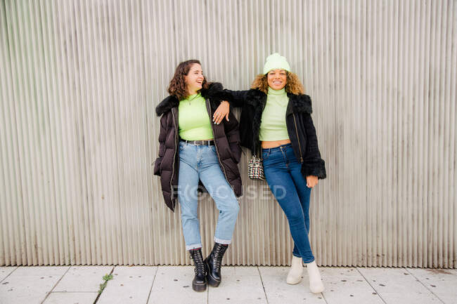 Мультиэтнические подруги развлекаются на улице, опираясь на стену. — стоковое фото