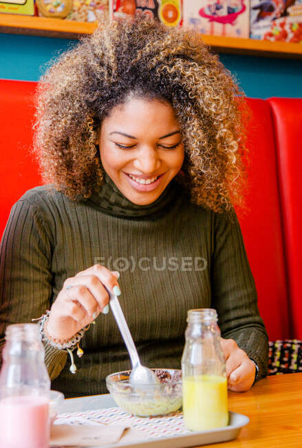 Retrato de una mujer afro con el pelo rizado comiendo en un bar - foto de stock