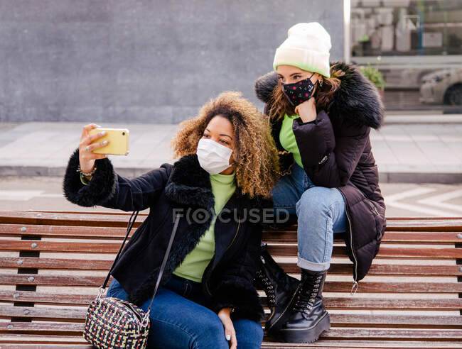 Zwei Freundinnen machen ein Selbstporträt mit dem Handy, während sie eine Schutzmaske auf der Straße tragen — Stockfoto