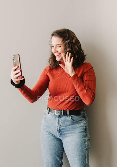 Woman making a video call while greeting next to a white wall — Stock Photo