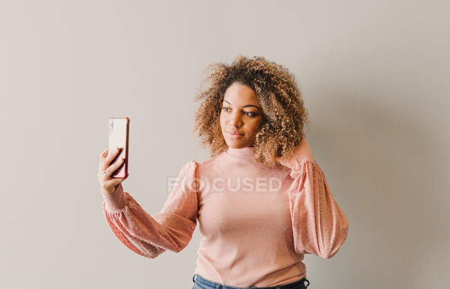 Afro mulher com cabelo encaracolado tomando um auto retrato ao lado de uma parede branca — Fotografia de Stock