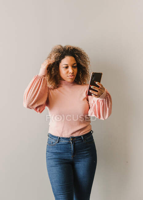 Afro donna con i capelli ricci prendendo un autoritratto accanto a un muro bianco — Foto stock