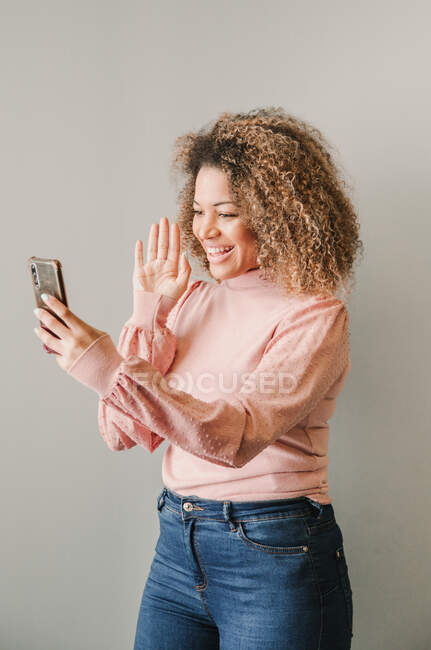 Afro woman making a video call while greeting next to a white wall — Stock Photo