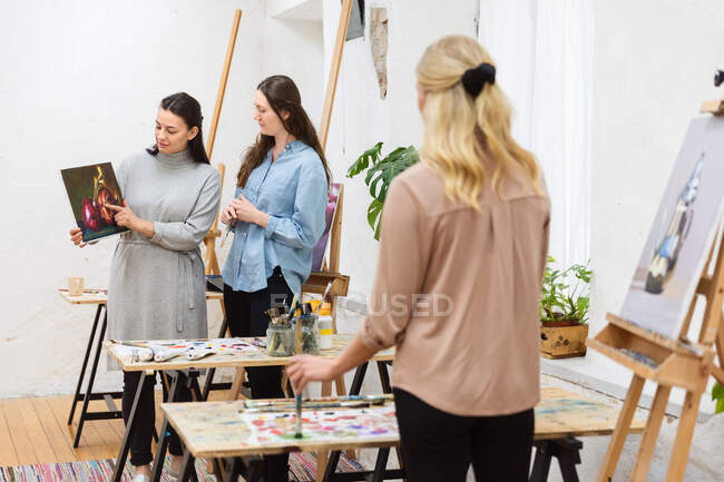 Group of female artists standing in creative studio and talking about painting during workshop — Stock Photo