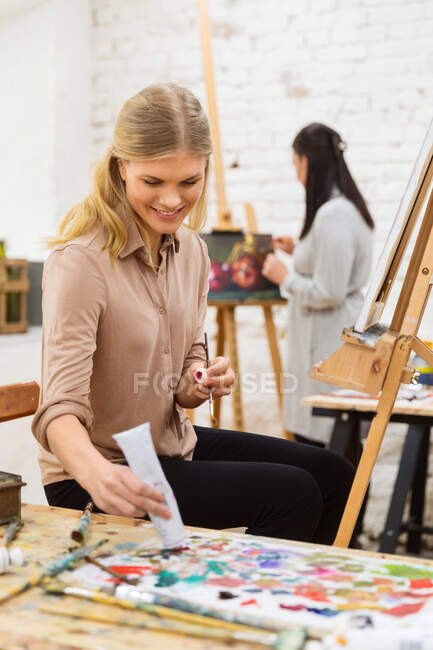 Allegro artista femminile utilizzando vernice e creando opere d'arte su tela in studio d'arte — Foto stock
