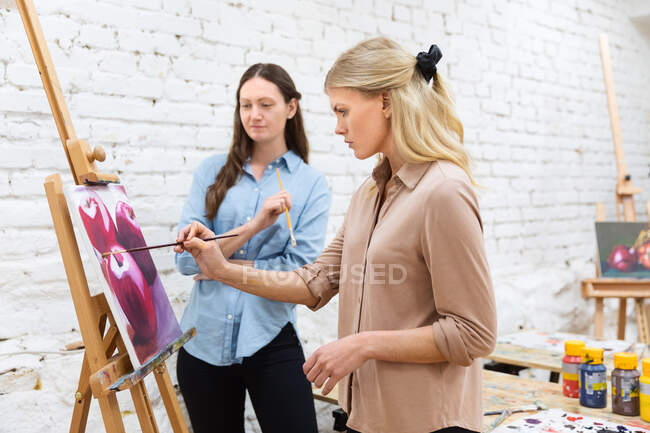 Vista lateral de artista femenina enseñando pintura de mujer en caballete durante el taller en estudio creativo - foto de stock