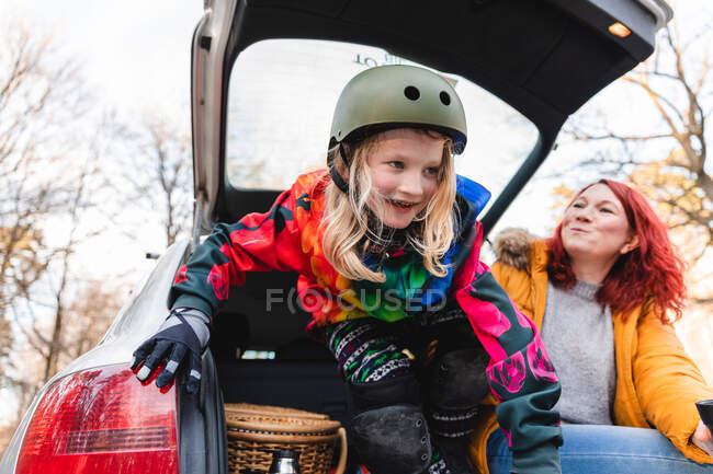 Знизу усміхнений підлітковий ковзаняр і мати сидять у багажнику припаркованої машини і розважаються у вихідні разом — стокове фото