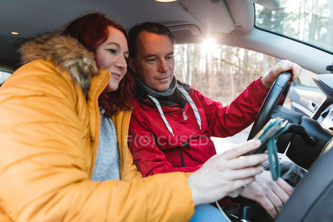 Vista laterale di coppia di viaggiatori seduti in auto e utilizzando la mappa GPS sul telefono cellulare durante il viaggio — Foto stock