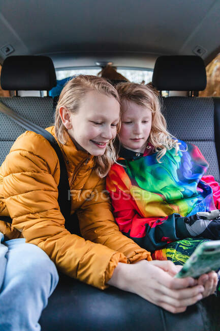 Захоплені сестри сидять в машині і грають цікаву гру на мобільному телефоні разом — стокове фото