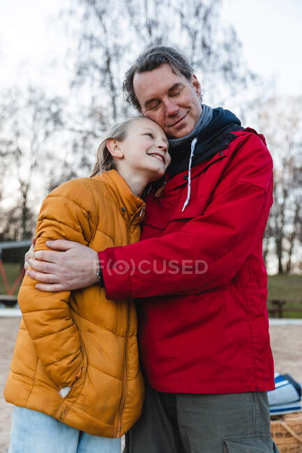 Cheerful tender father and teenage girl hugging while standing in autumn park and enjoying weekend — Stock Photo