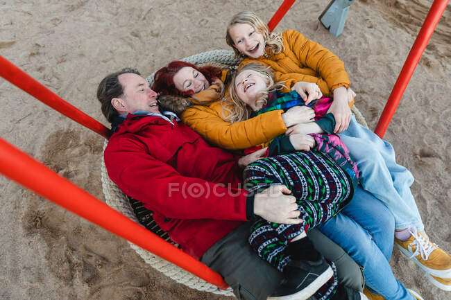From above of delighted family riding net swing on playground in autumn park and having fun together — Stock Photo