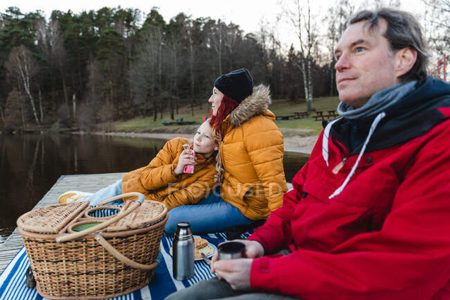 Loving family with teenage daughter relaxing on wooden quay and enjoying picnic in autumn forest — Stock Photo