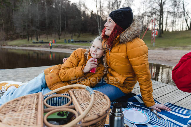 Loving family with teenage daughter relaxing on wooden quay and enjoying picnic in autumn forest — Stock Photo