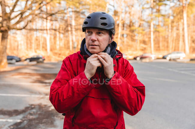 Дорослий чоловік одягає захисний шолом, стоячи в парку восени у вихідні — стокове фото