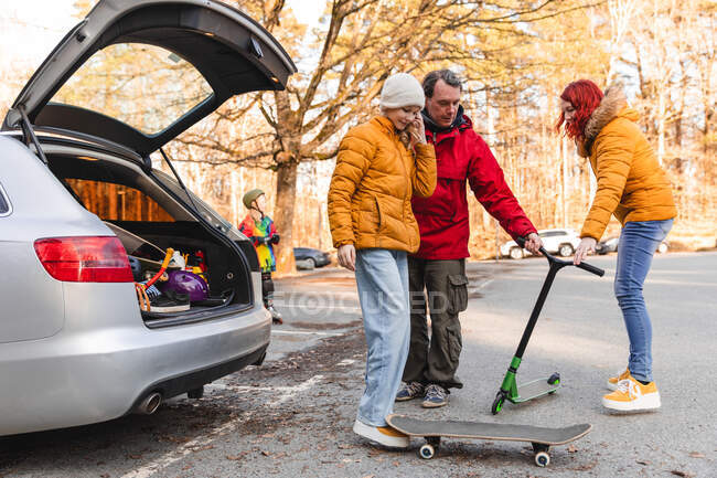 Padre e adolescente che prendono skateboard e scooter dal bagagliaio dell'auto per divertirsi insieme nel parco autunnale — Foto stock