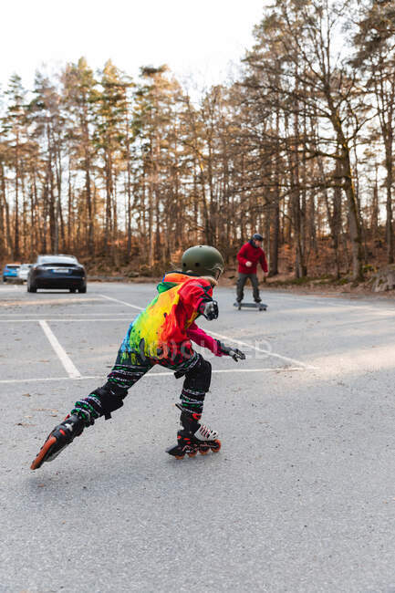 Vista posterior de niño anónimo activo en el casco patinaje sobre el aparcamiento en el parque de otoño y divertirse - foto de stock