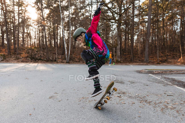 Vista lateral del talentoso skater adolescente saltando con el monopatín en el parque en otoño - foto de stock