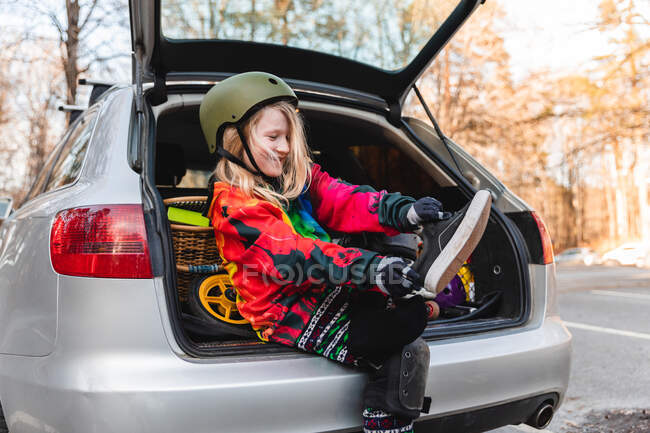 Delighted girl in protective helmet taking off sneakers and preparing for rollerblading in autumn park — Stock Photo
