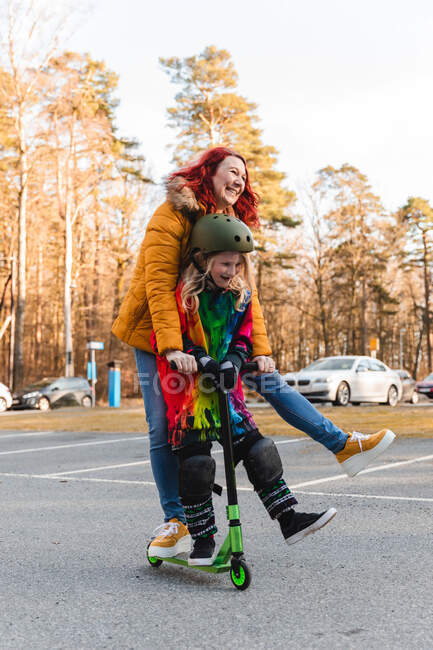 Deliziosa madre e figlia cavalcando scooter calcio sul parcheggio divertendosi durante il fine settimana in autunno — Foto stock
