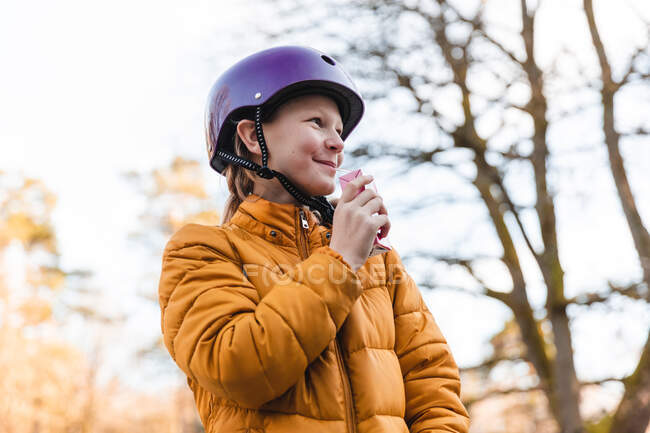 From below of content teenage girl in helmet standing in park in fall and enjoying sweet juice with straw — Stock Photo