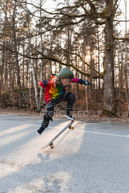 Енергетична дівчина-підліток в захисному спорядженні стрибає над землею зі скейтбордом і виконує трюк — стокове фото