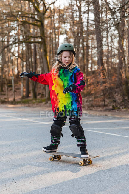 Adolescente enérgica en equipo de protección montando sobre el suelo con monopatín - foto de stock