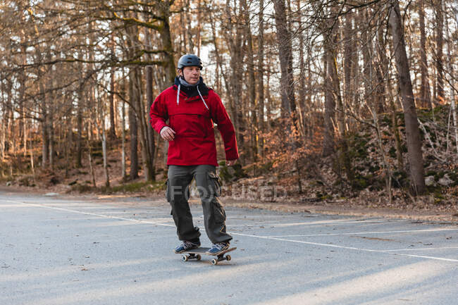 Father in helmet riding skateboard on parking in autumn park — Stock Photo