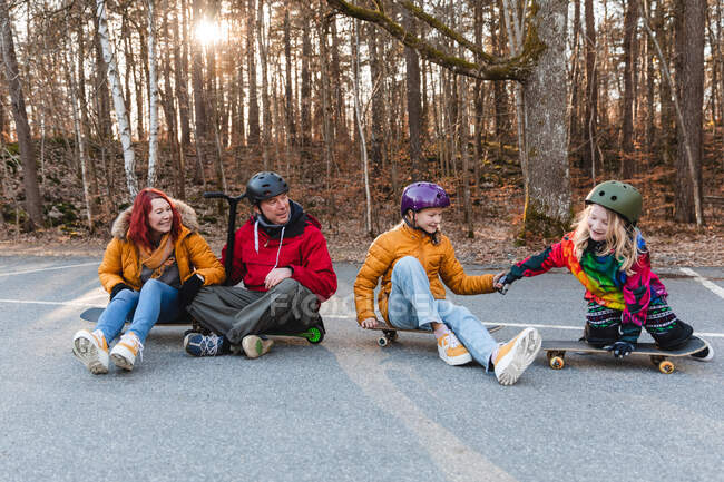 Alegre familia sentada en monopatines y patada scooter mientras disfruta de fin de semana y divertirse en el parque de otoño - foto de stock