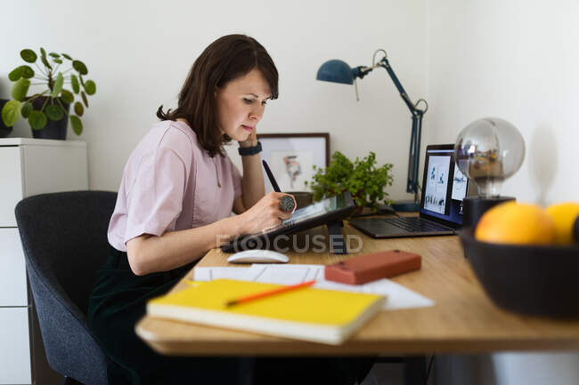 Вид збоку жінки малює зображення на графічному планшеті, сидячи за столом в домашньому офісі — стокове фото
