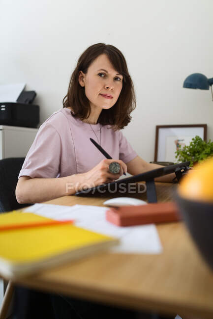 Vista lateral de la mujer dibujo de la imagen en la tableta gráfica mientras está sentado en la mesa en la oficina en casa - foto de stock