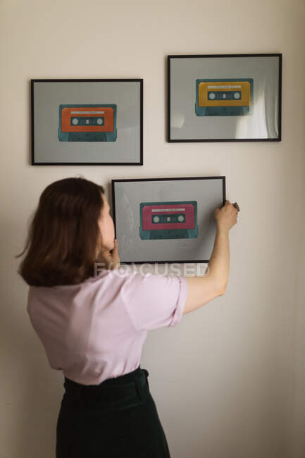Anonymous female adjusting frame with cassette tape picture on beige wall at home — Stock Photo