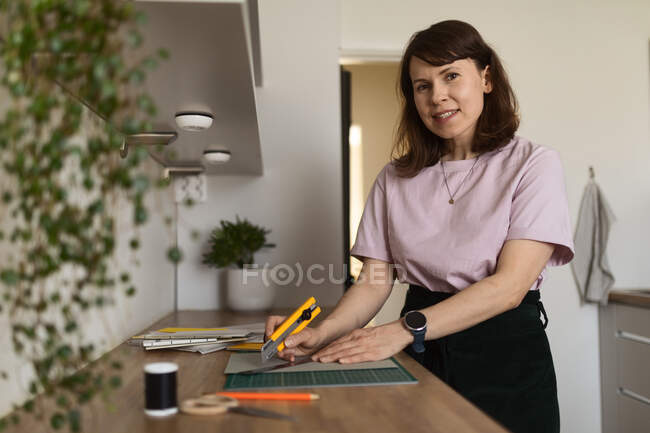 Dibujo de dibujo del diseñador gráfico femenino contenido en papel mientras está de pie en la mesa en casa y trabajando de forma remota - foto de stock