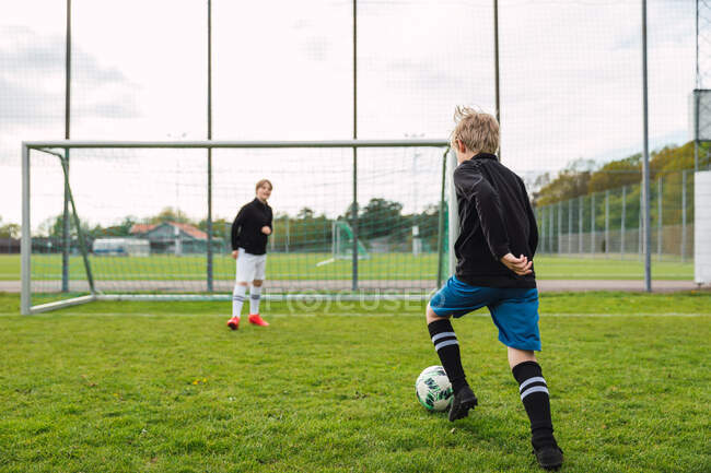 Хлопчики-підлітки в спортивному одязі грають у футбол разом на зеленому полі влітку — стокове фото
