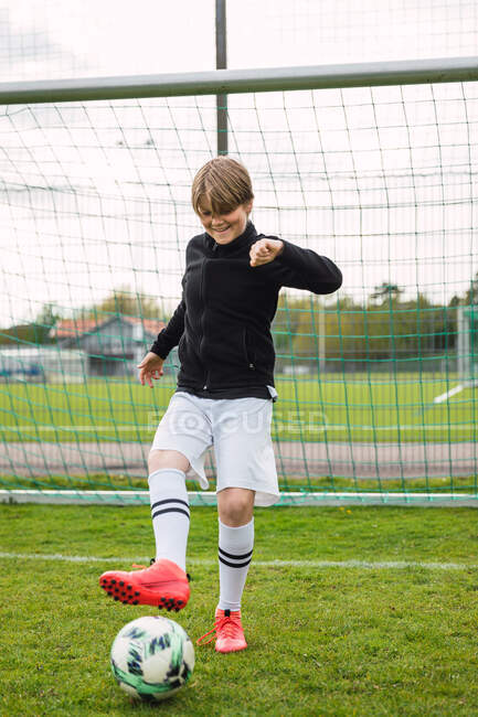 Delighted teenage boy in sportswear standing with ball on football field near net — Stock Photo