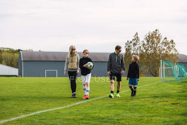 Весела пара і сини-підлітки в спортивному одязі збираються в зеленому футбольному полі для гри в футбол разом у вихідні — стокове фото