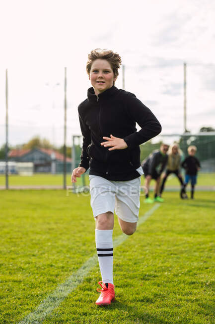 Веселый футболист-подросток в спортивной одежде и сапогах, бегающий по полю во время тренировок летом — стоковое фото